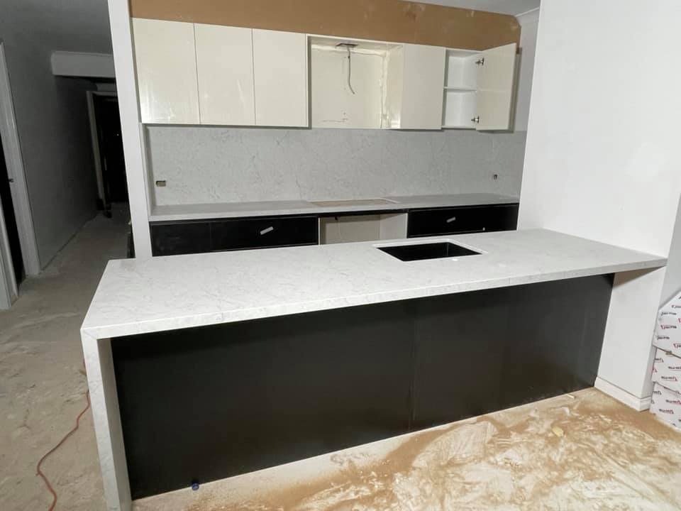 Kitchen with a white speckled stone island benchtop and black cabinets