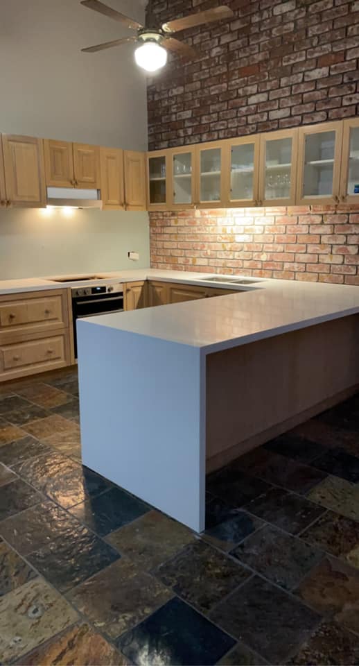 White stone waterfall island beside an exposed brick wall and slate floor