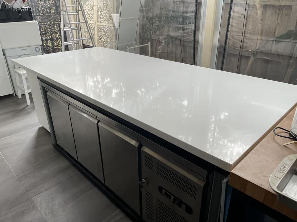 Side view of a white stone island benchtop over stainless steel fridges