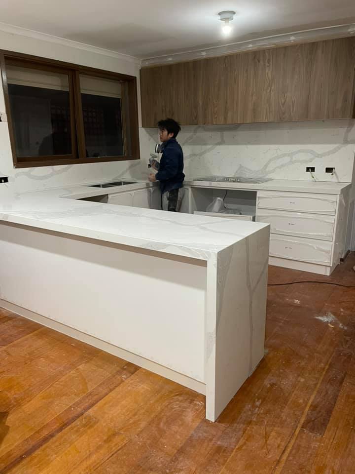Kitchen island with a white waterfall stone benchtop, installer in the background