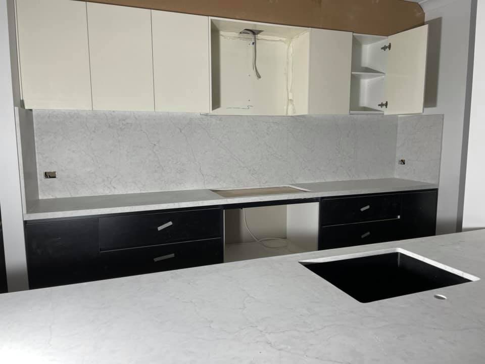 Pale grey marble-look benchtop and full-height splashback above black drawers