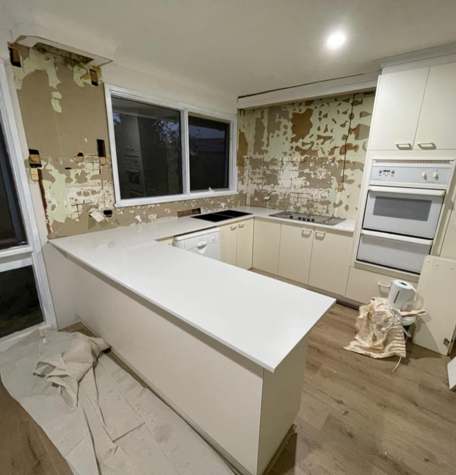 U-shaped kitchen with a white stone benchtop, walls stripped for renovation