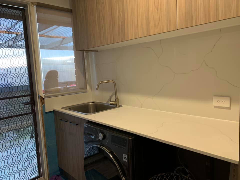 Laundry with a white veined stone benchtop and splashback above a washing machine