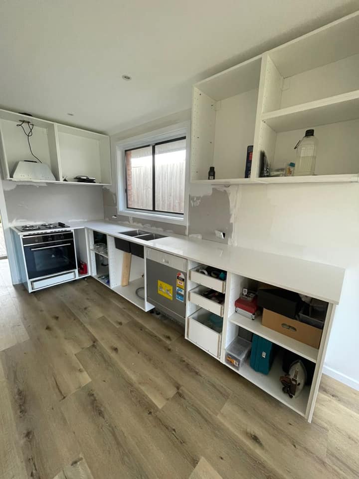 White stone benchtops on unfinished cabinets in a kitchen with a timber floor