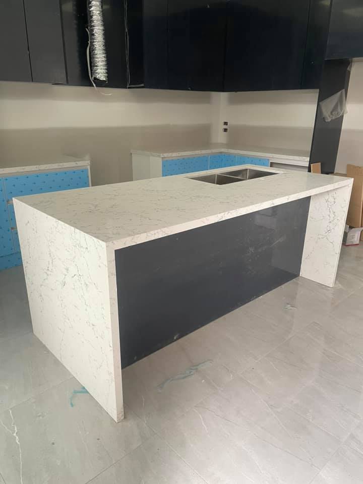 Kitchen island with a white speckled stone top and waterfall ends