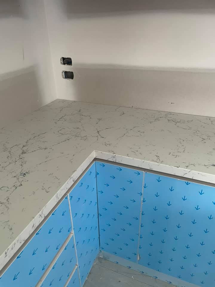Corner benchtop in white veined stone on cabinets in blue protective film