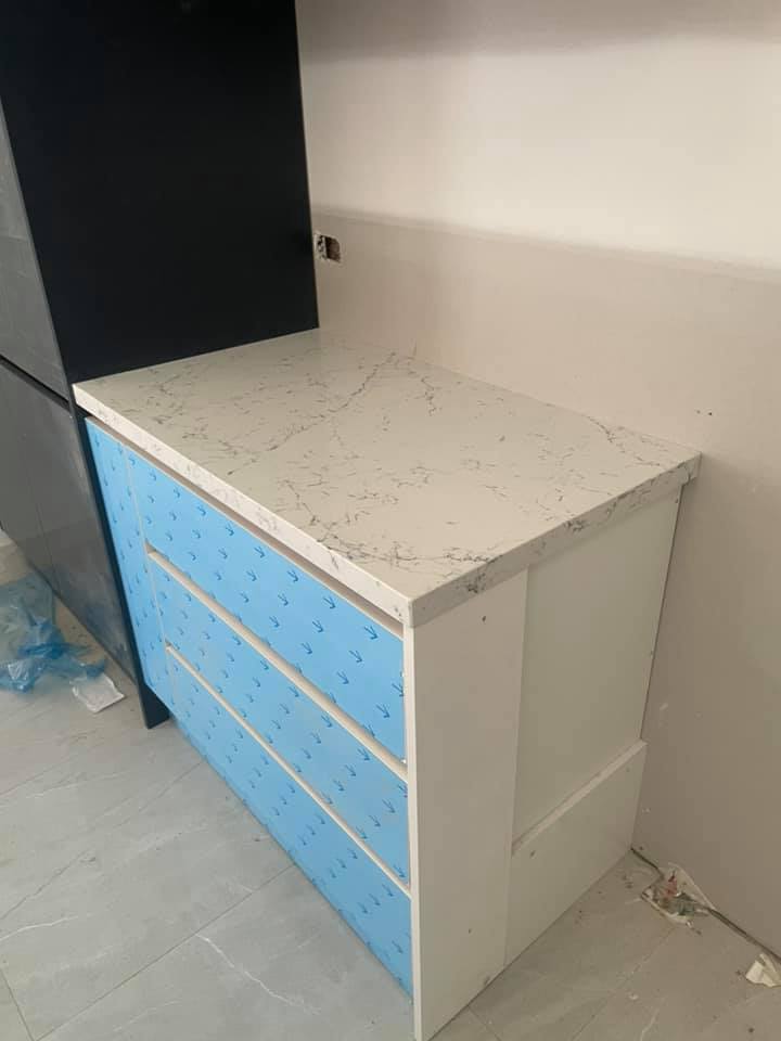Small white veined stone benchtop on a cabinet in blue protective film