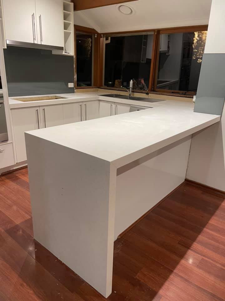 White stone peninsula benchtop with a waterfall end on a timber floor