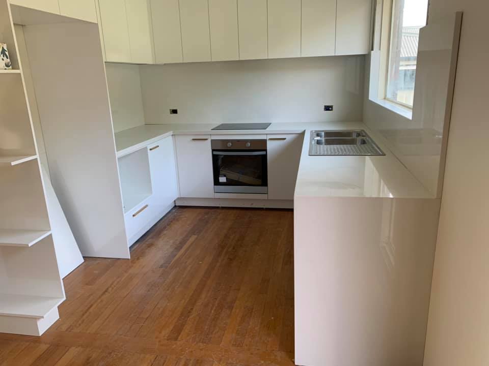 White U-shaped kitchen with stone benchtops and a waterfall end, seen from the doorway