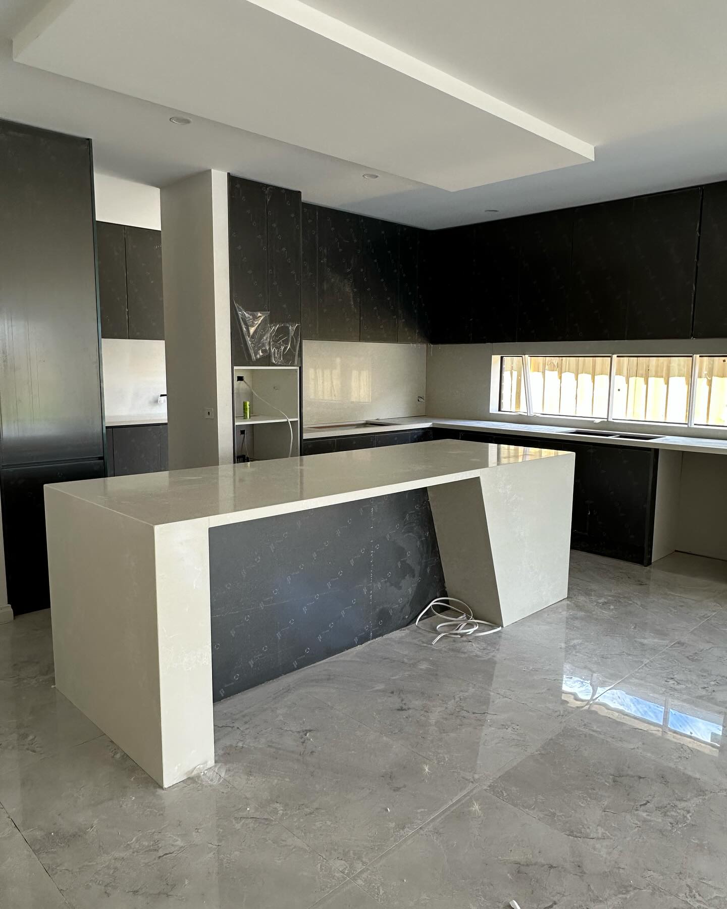 White stone waterfall island with a dark marble front panel and black cabinets