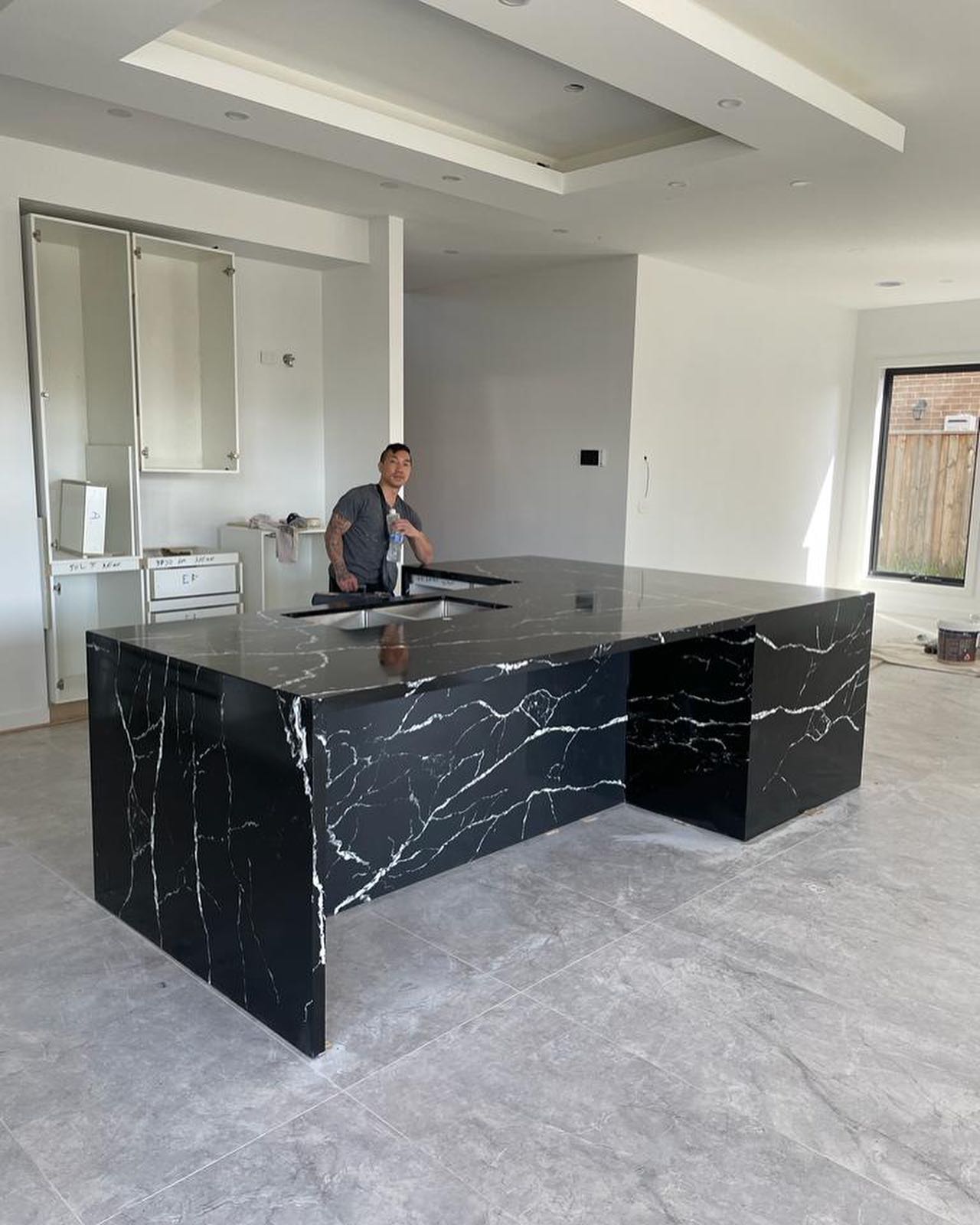 Black marble-look waterfall island with white veining, worker in the background