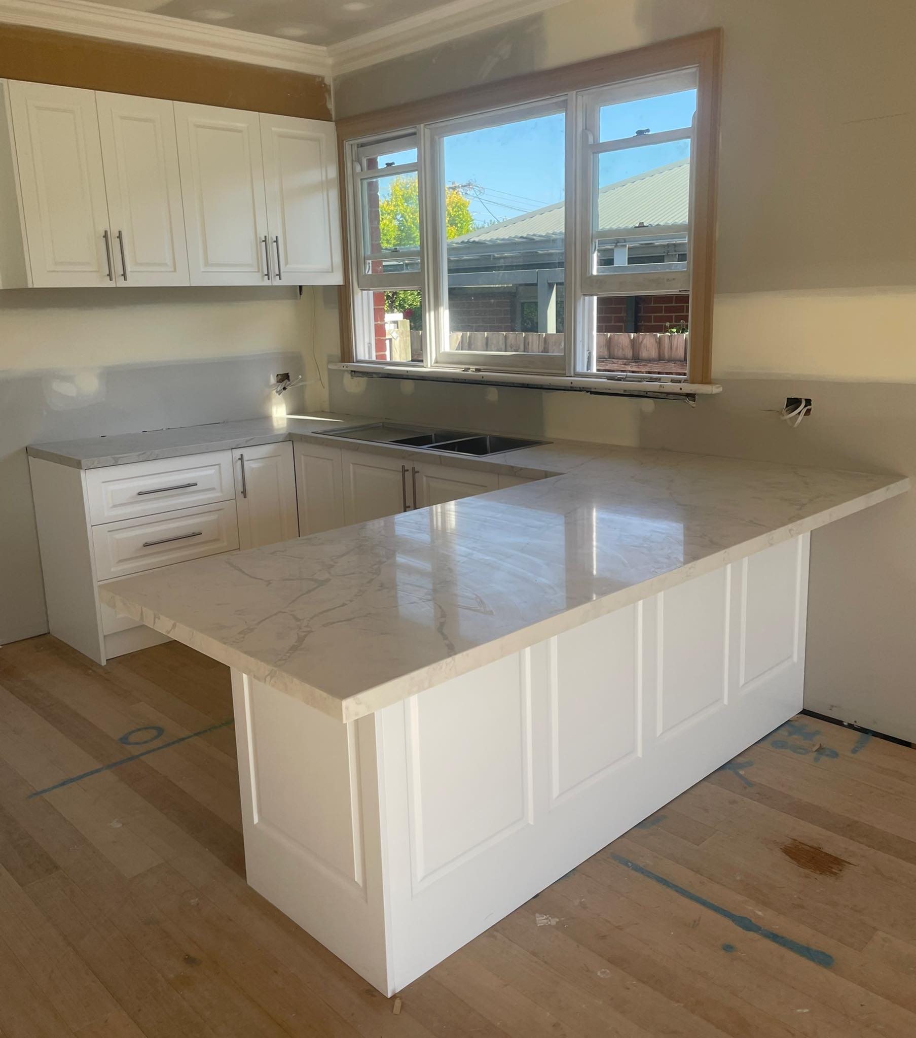 L-shaped kitchen with a pale marble-look benchtop on white shaker cabinets