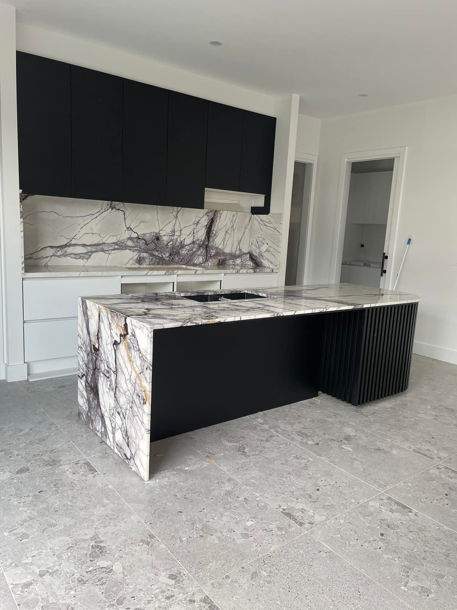Wider view of a purple-veined marble waterfall island and splashback with black cabinets