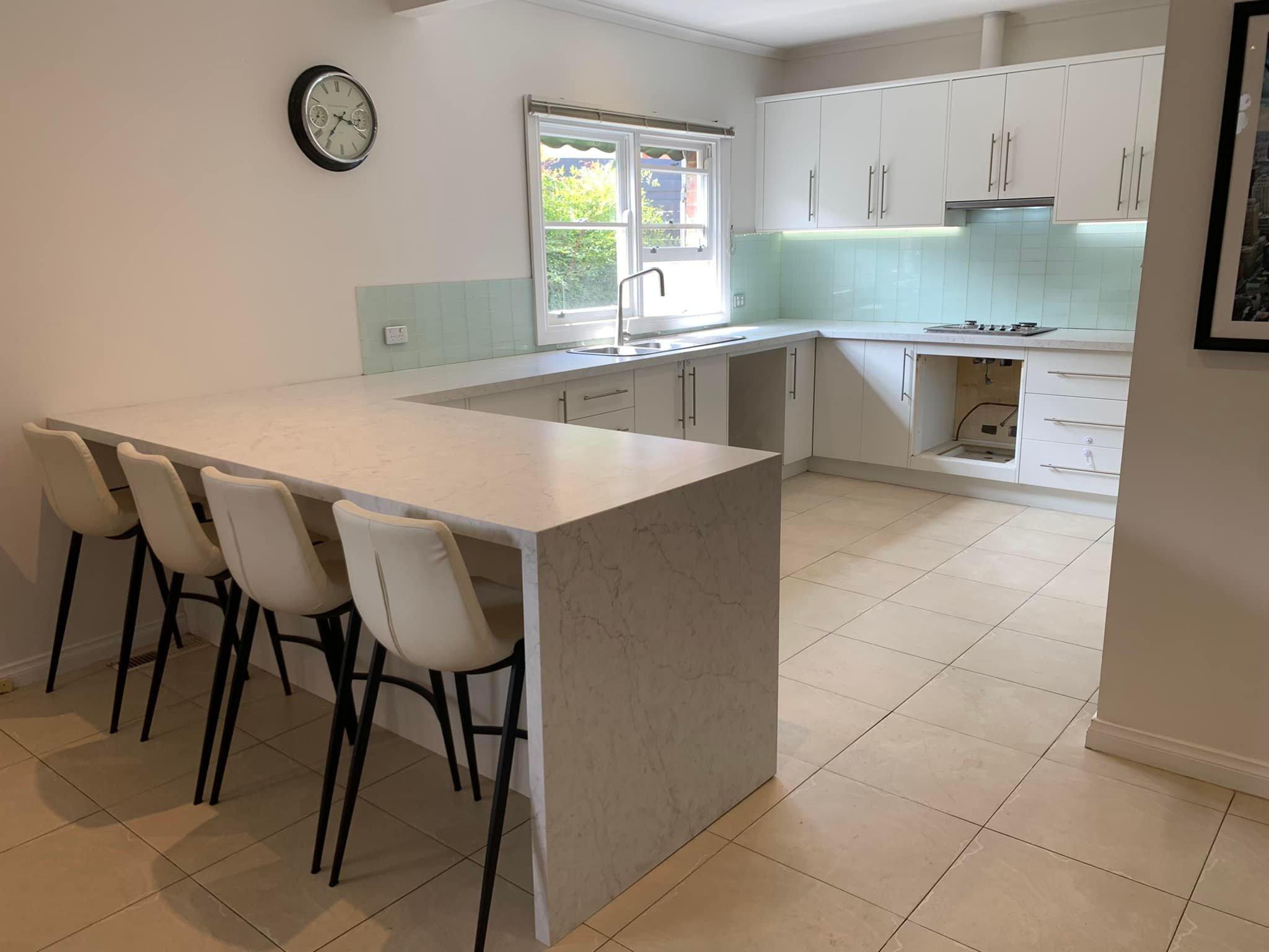 Grey stone peninsula benchtop with a waterfall end and four white bar stools