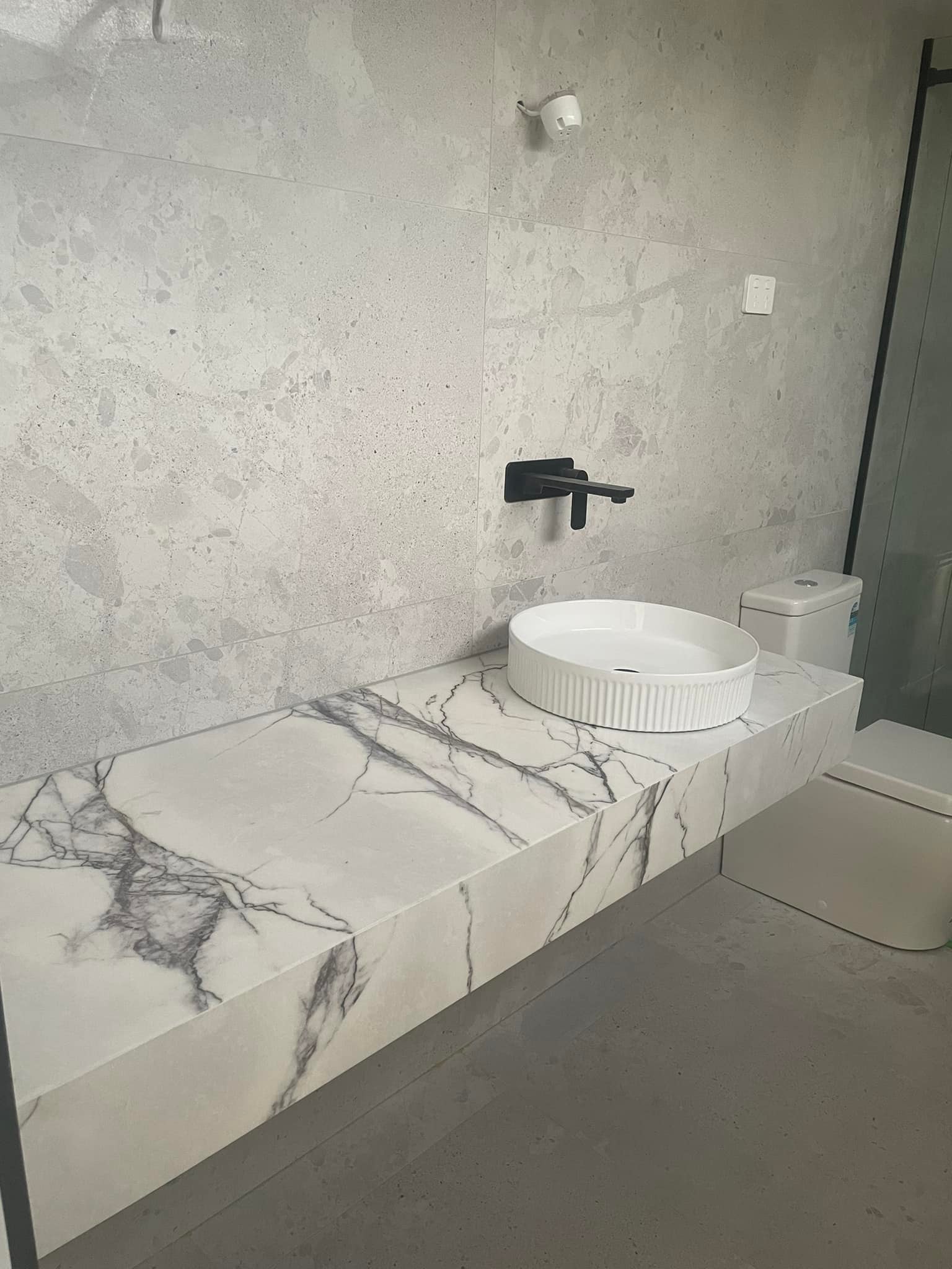 Long floating vanity in purple-veined marble with a round basin beside a toilet