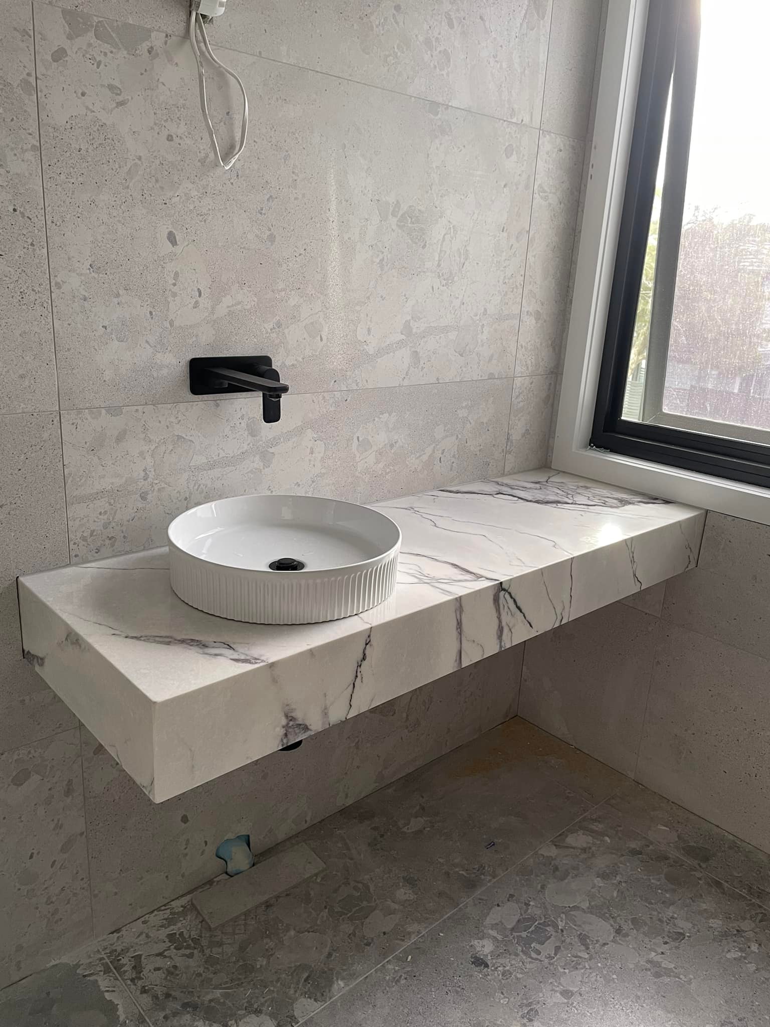 Floating purple-veined marble vanity with a round basin beside a window