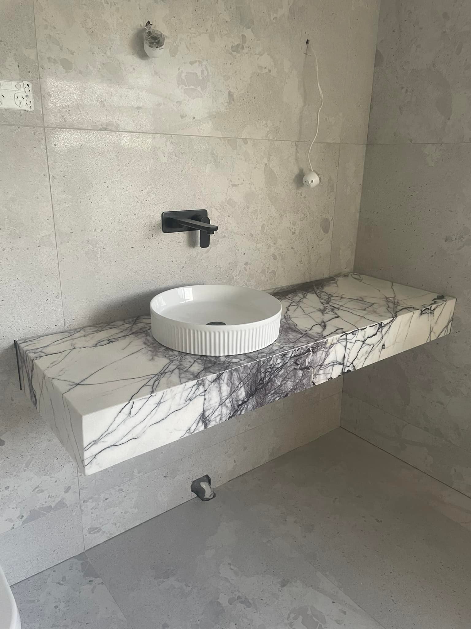 Portrait view of a floating purple-veined marble vanity with a black wall tap