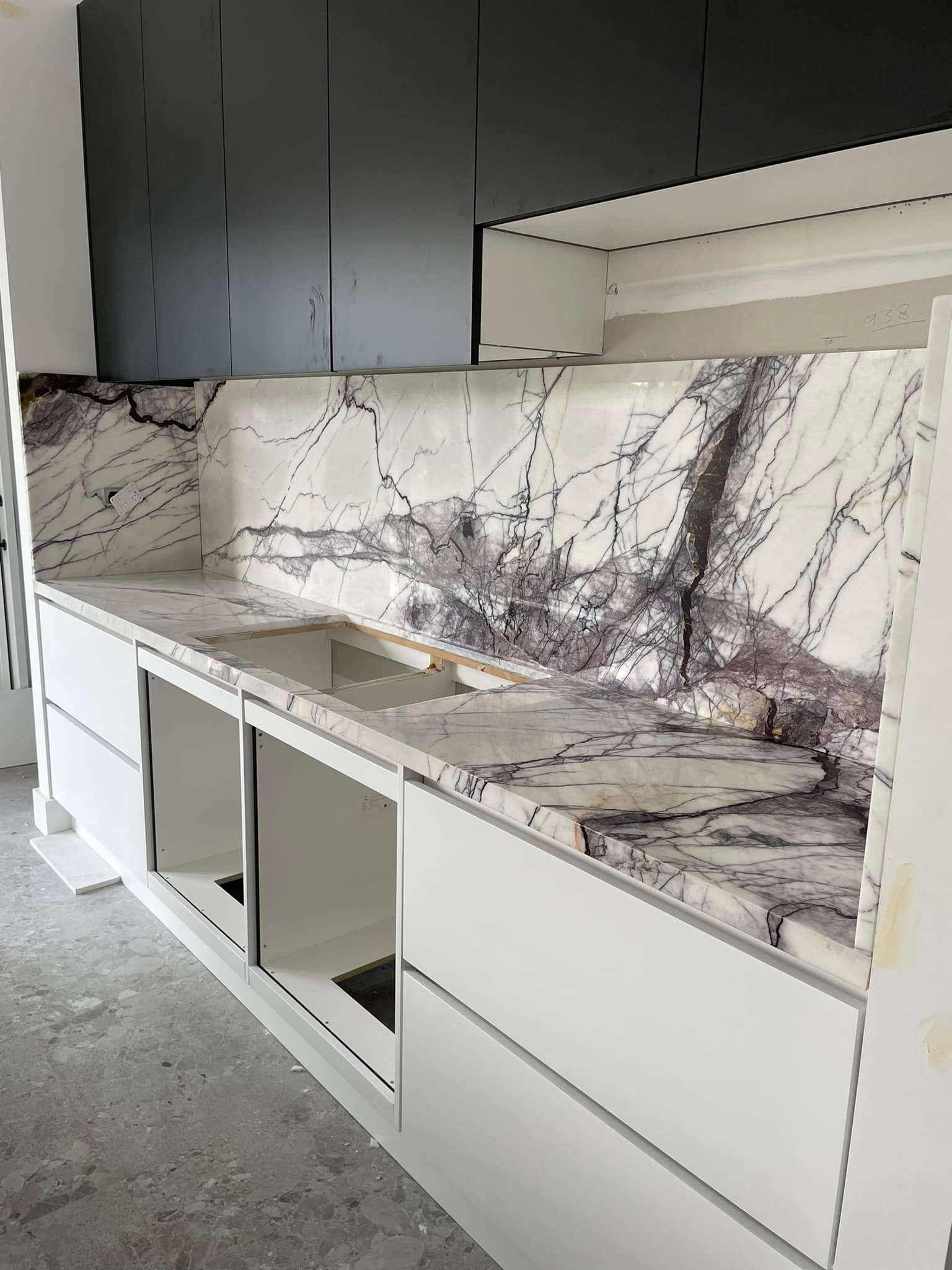 Long purple-veined marble benchtop and splashback under black cabinets