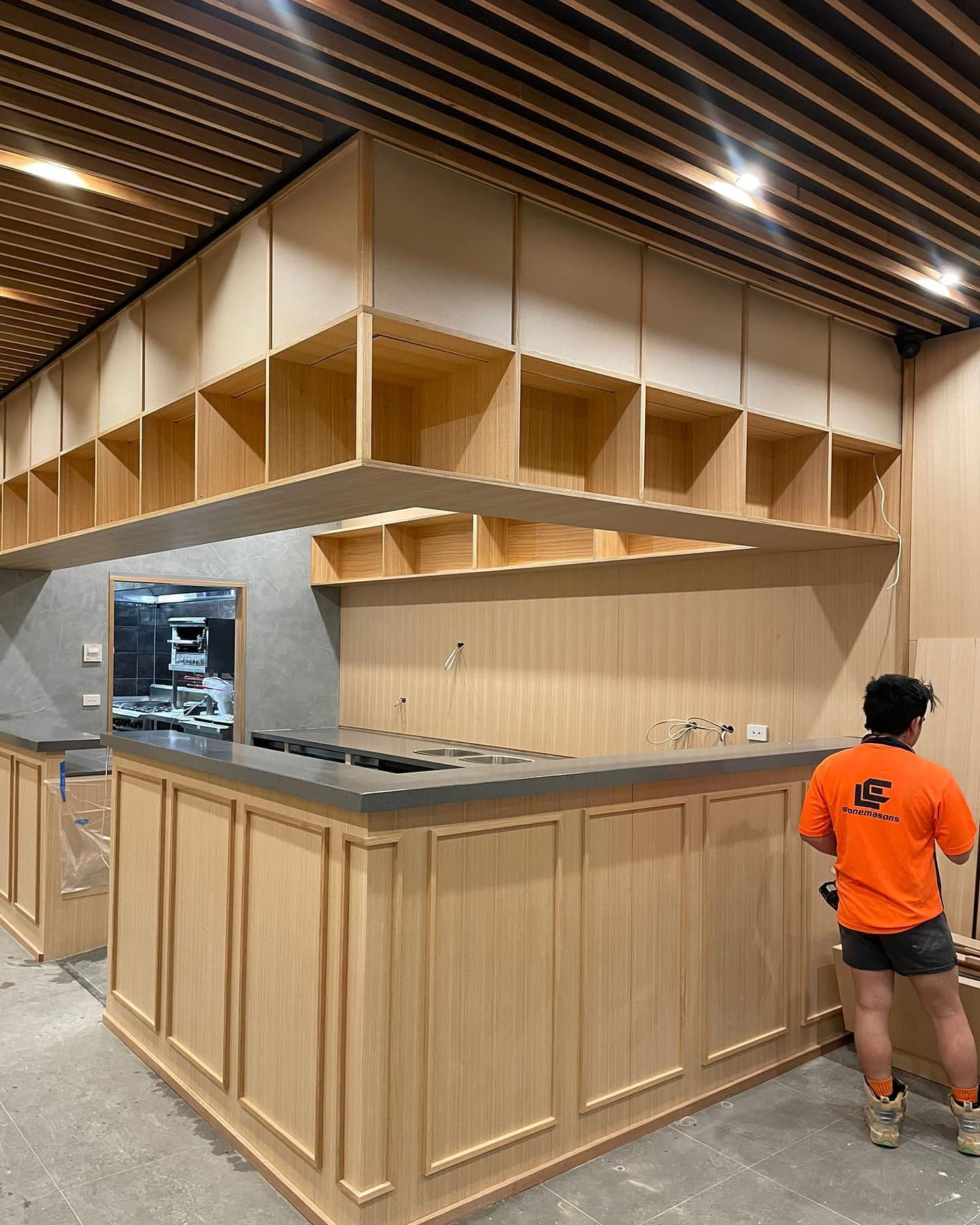 Commercial fit-out with a grey stone counter on timber cabinetry, worker in orange