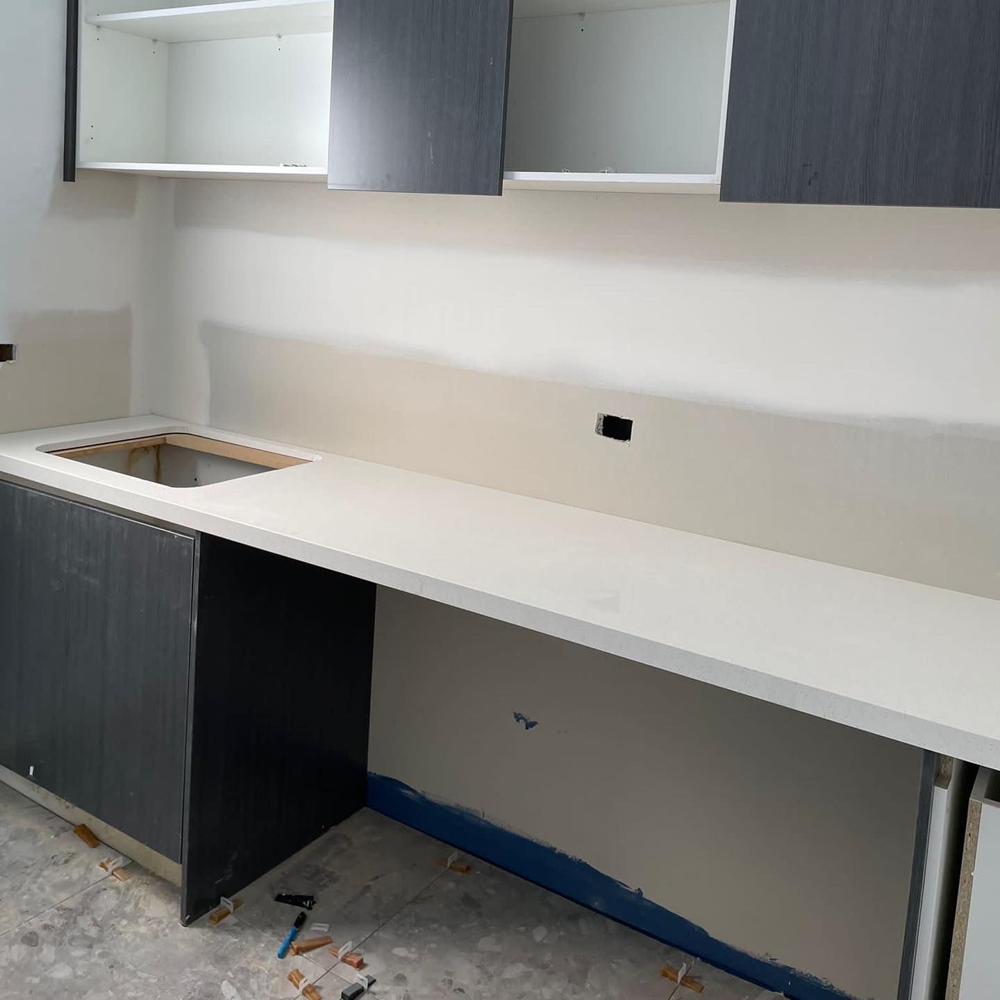 White stone benchtop with a sink cut-out on dark cabinets