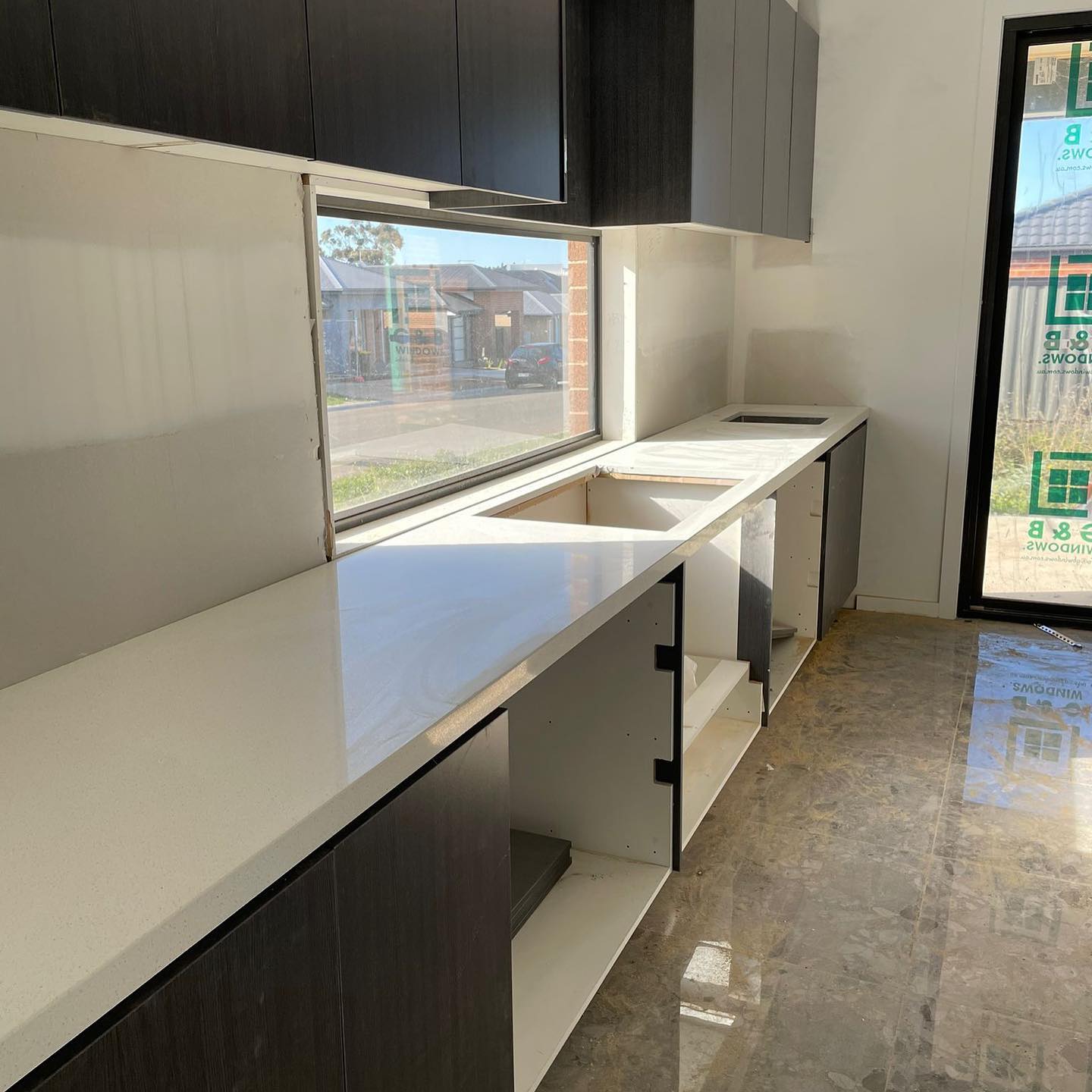 Long white stone benchtop on dark cabinets beside a window