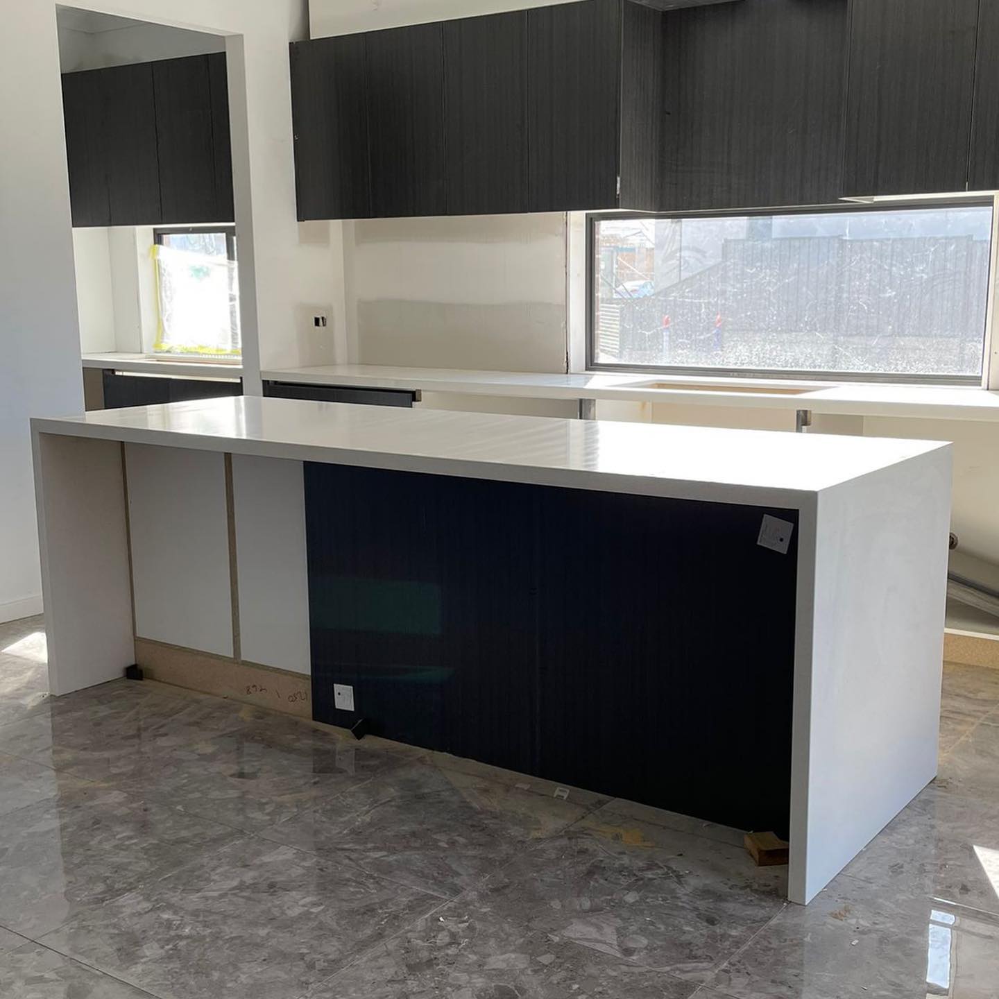 Kitchen island with a white stone top, waterfall ends and a black panel