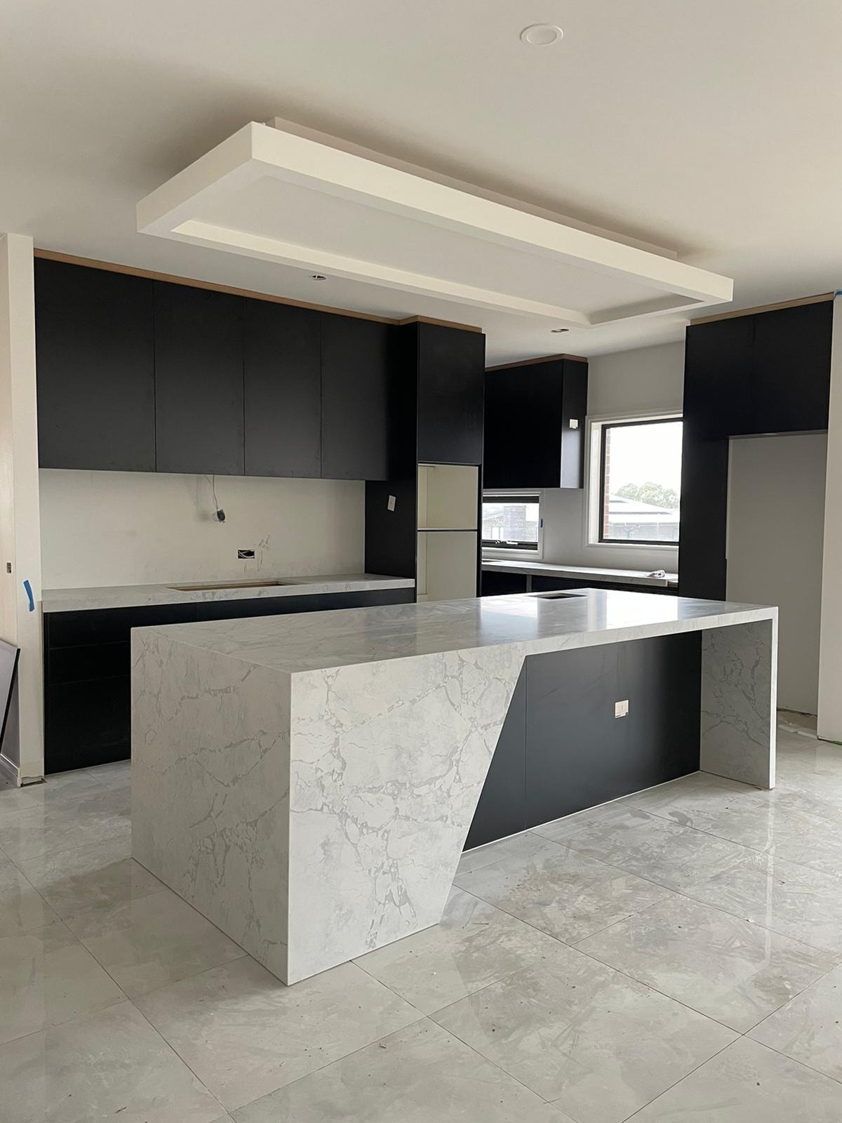 Marble-look waterfall island with an angled black panel under a bulkhead