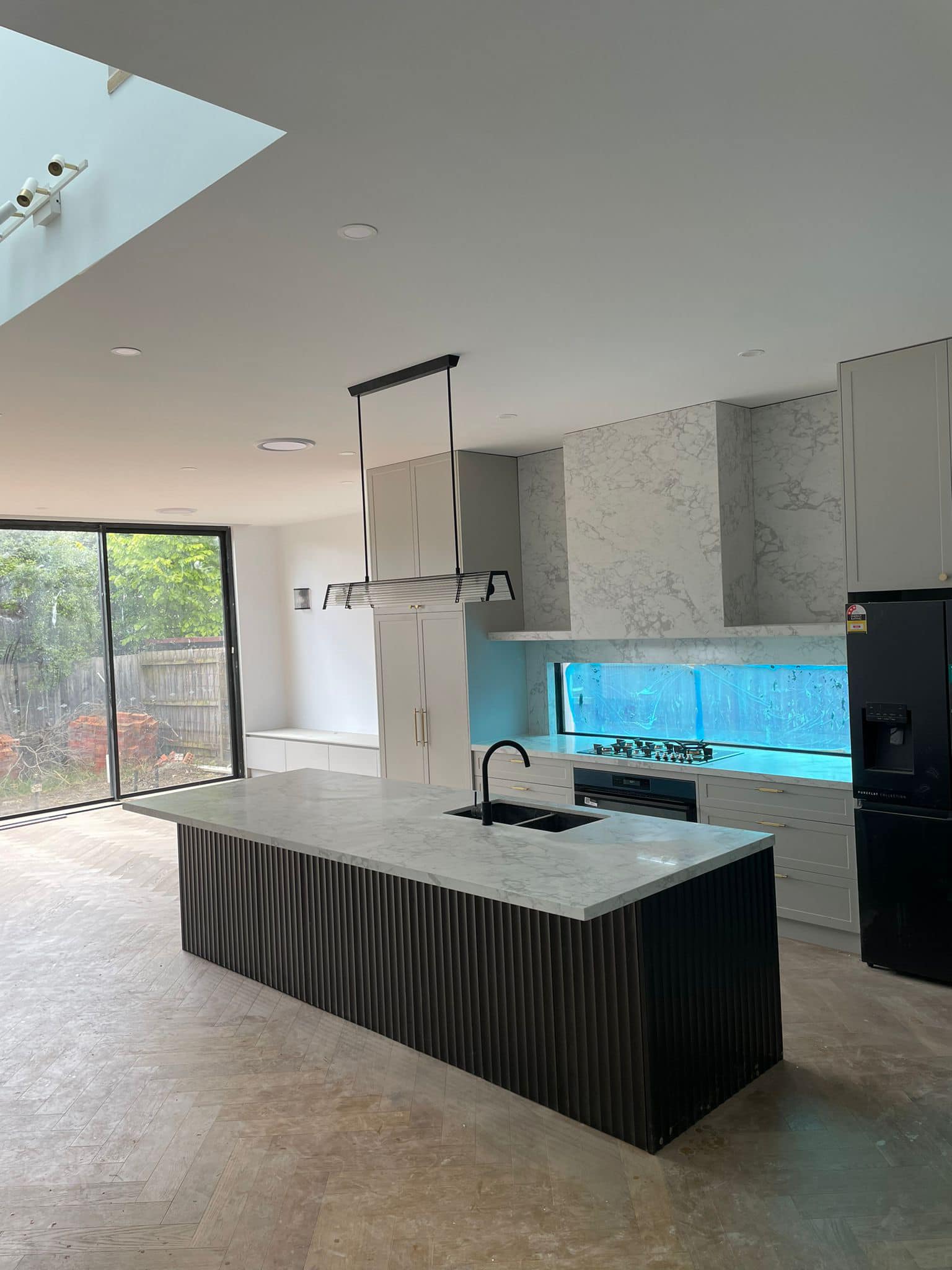Wider view of a kitchen island with a grey marble top and black fluted panels