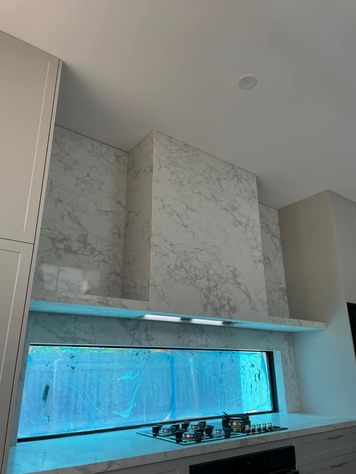 White marble-look stone rangehood cover and splashback above a cooktop