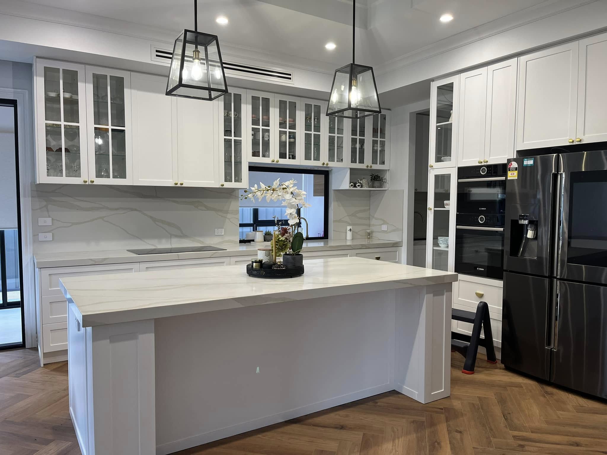 Kitchen island with a white stone top under glass pendant lights