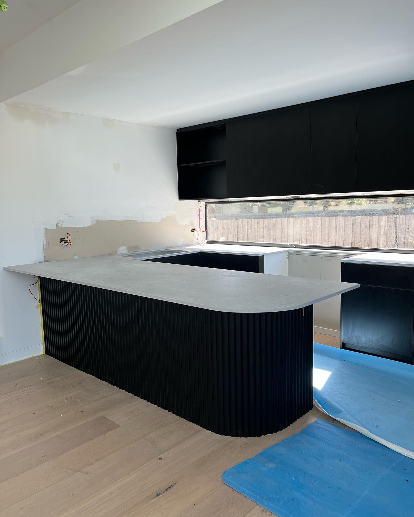 Curved kitchen island with a pale stone top and black fluted base