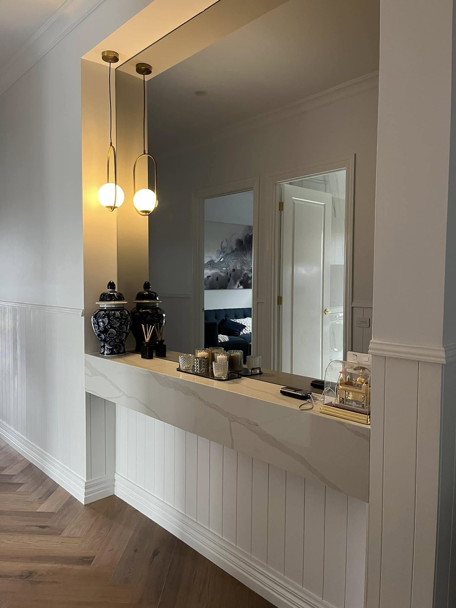 Stone-topped vanity desk under a large mirror and pendant lights