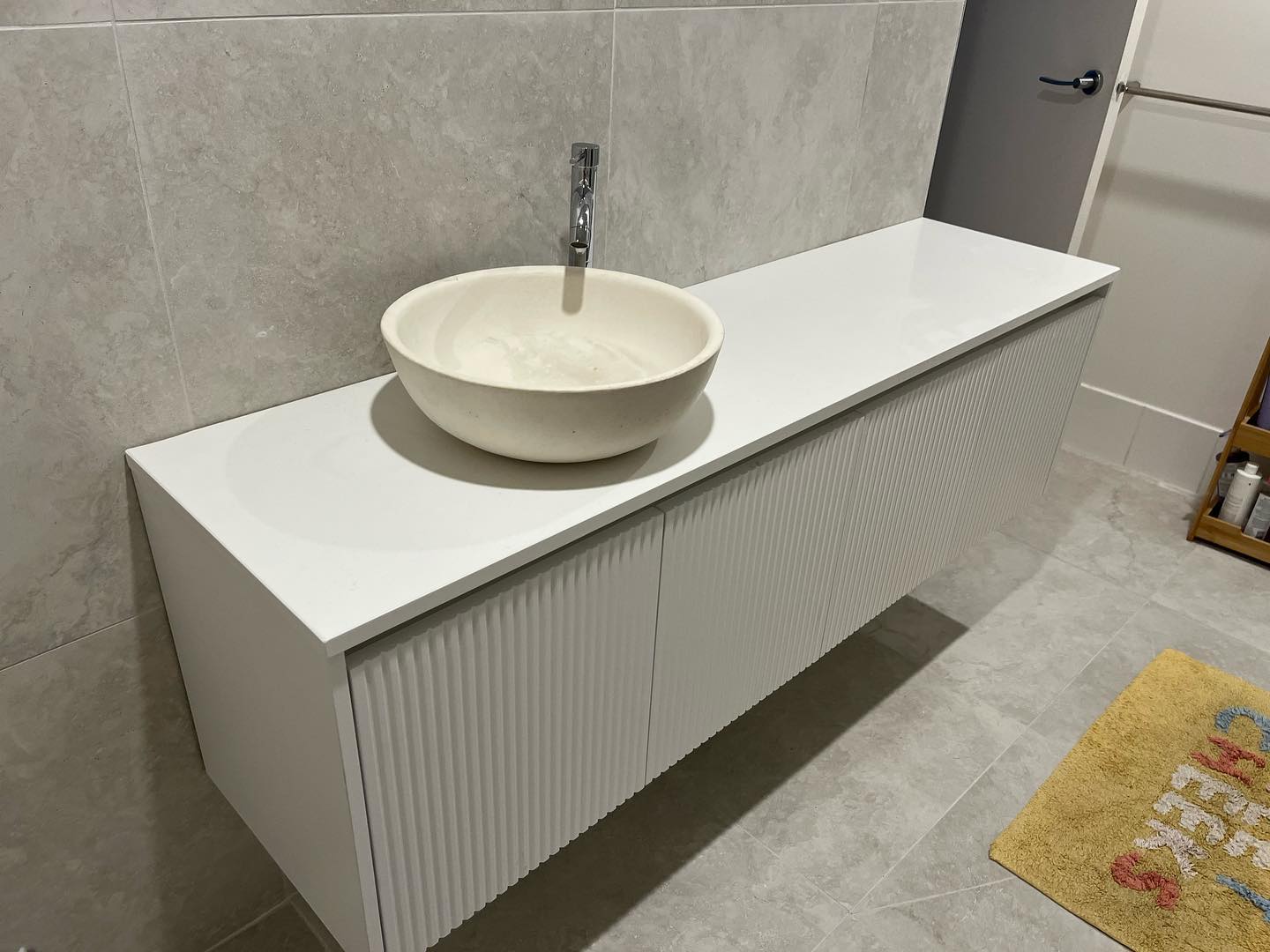 Floating fluted vanity with a white stone top and round vessel basin