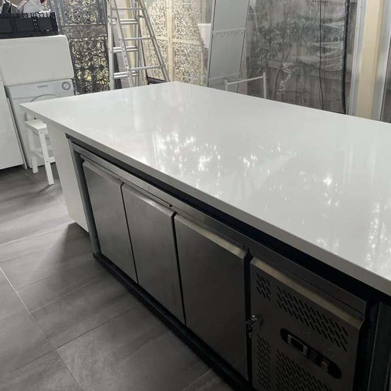 White stone benchtop on a large island over stainless steel fridges